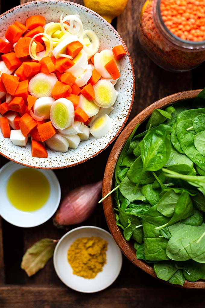 Zutaten für das  Rote Linsen-Curry in unterschiedlich großen Schalen und Behältern. Zu sehen sind: geschnittenes Suppengemüse, rote Linsen, Zitrone, Blattspinat, Gewürze und Schalotten.