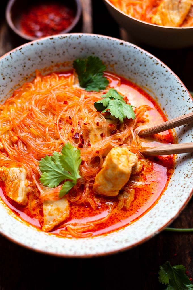 Thai Suppe mit Hähnchen und Kokosmilch in einer Schüssel. Dekoriert mit Koriander und serviert mit Stäbchen.