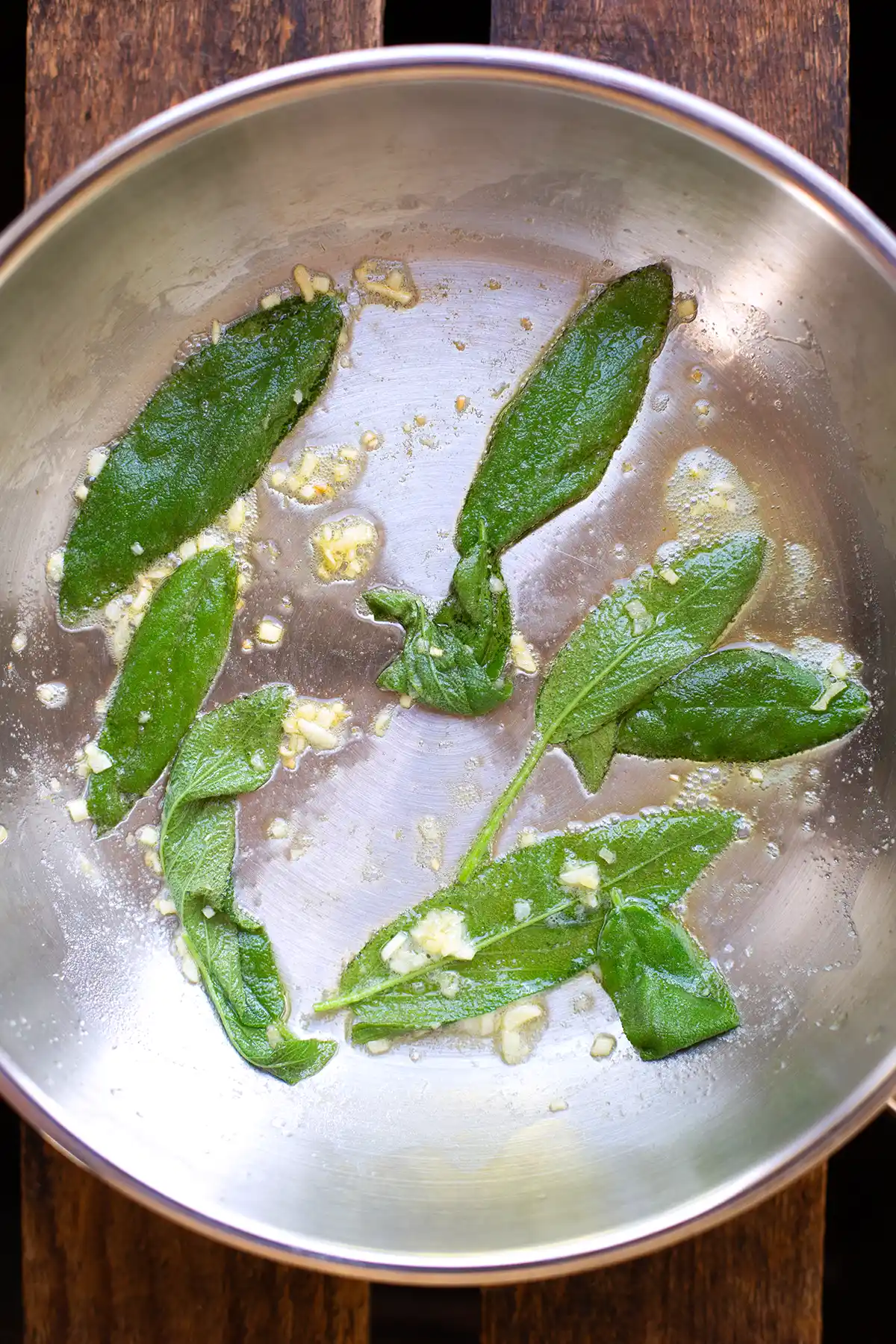 Frischer Salbei und Knoblauch werden mit Butter in einer silbernen Pfanne angebraten.