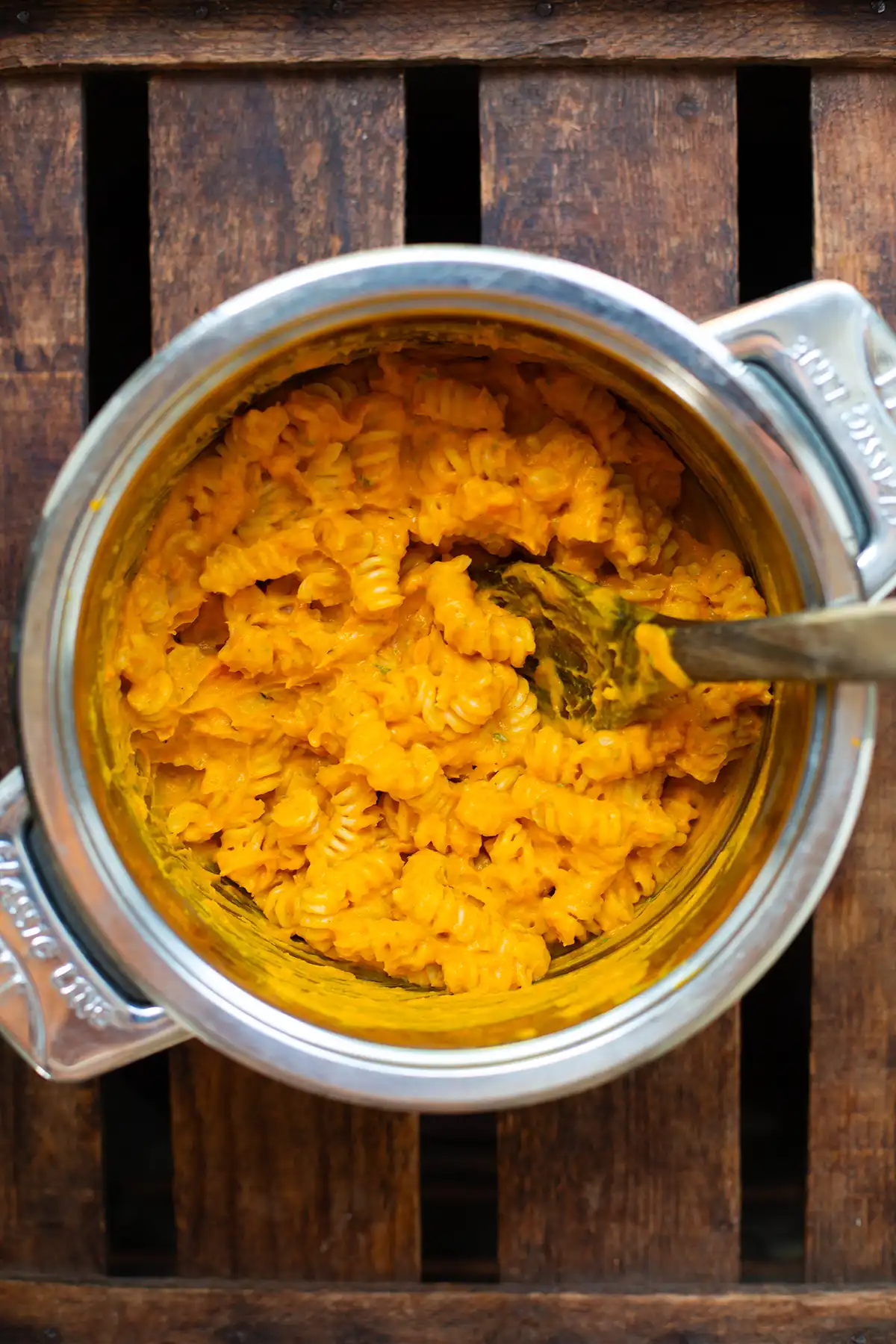 Kürbis-Sauce mit Fusilli in einem silbernen Topf vermischt. Der Topf steht auf einem dunklen Holzuntergrund.