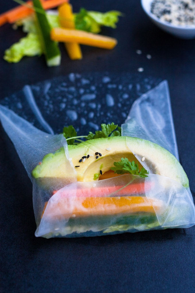 Werbung. Summer Rolls mit schneller Erdnusssauce. Frisch, knackig und gesund! Perfekt als leichtes Abendessen und zum Mitnehmen - kochkarussell.com Zutaten für die Sommerrollen (Avocado, Paprika, Gurke und Petersilie) in einem Reispapier, das schon zur Hälfte gefaltet, oben aber noch offen ist.