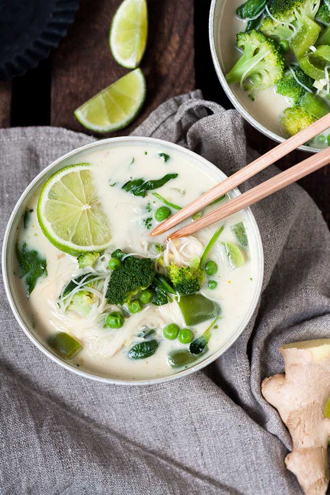20-Minuten Thai Green Curry Soup. Dieses 10-Zutaten Rezept ist herzhaft, würzig und schnell gemacht. Das perfekte, dampfende Soulfood nach einem langen Tag - kochkarussell.com Zwei Schüsseln der 20-Minuten Thai Green Curry Soup. Die Suppe ist in der einen Schüssel garniert mit zwei hellbraunen Ess-Stäbchen und einer Limettenscheibe.