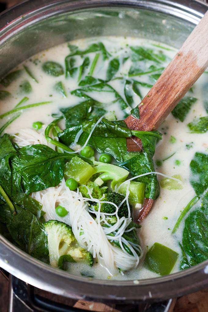 20-Minuten Thai Green Curry Soup. Dieses 10-Zutaten Rezept ist herzhaft, würzig und schnell gemacht. Das perfekte, dampfende Soulfood nach einem langen Tag - kochkarussell.com Thai Green Curry Soup mit eallen Zutaten in einem silbernen Topf wird gerade mit einem großen Holzlöffel umgerührt.