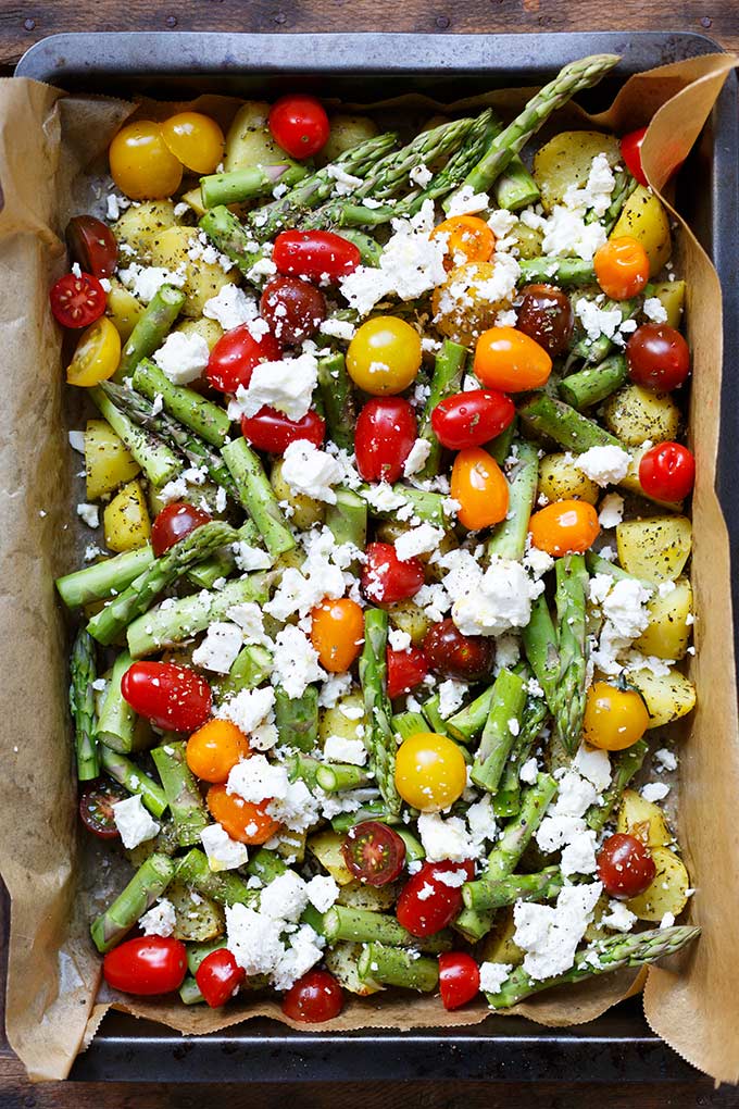 Alle Zutaten für die Ofenkartoffeln mit grünem Spargel, Tomaten und Feta auf einem Backblech mit Backpapier. Bereit, um in den Ofen geschoben zu werden.