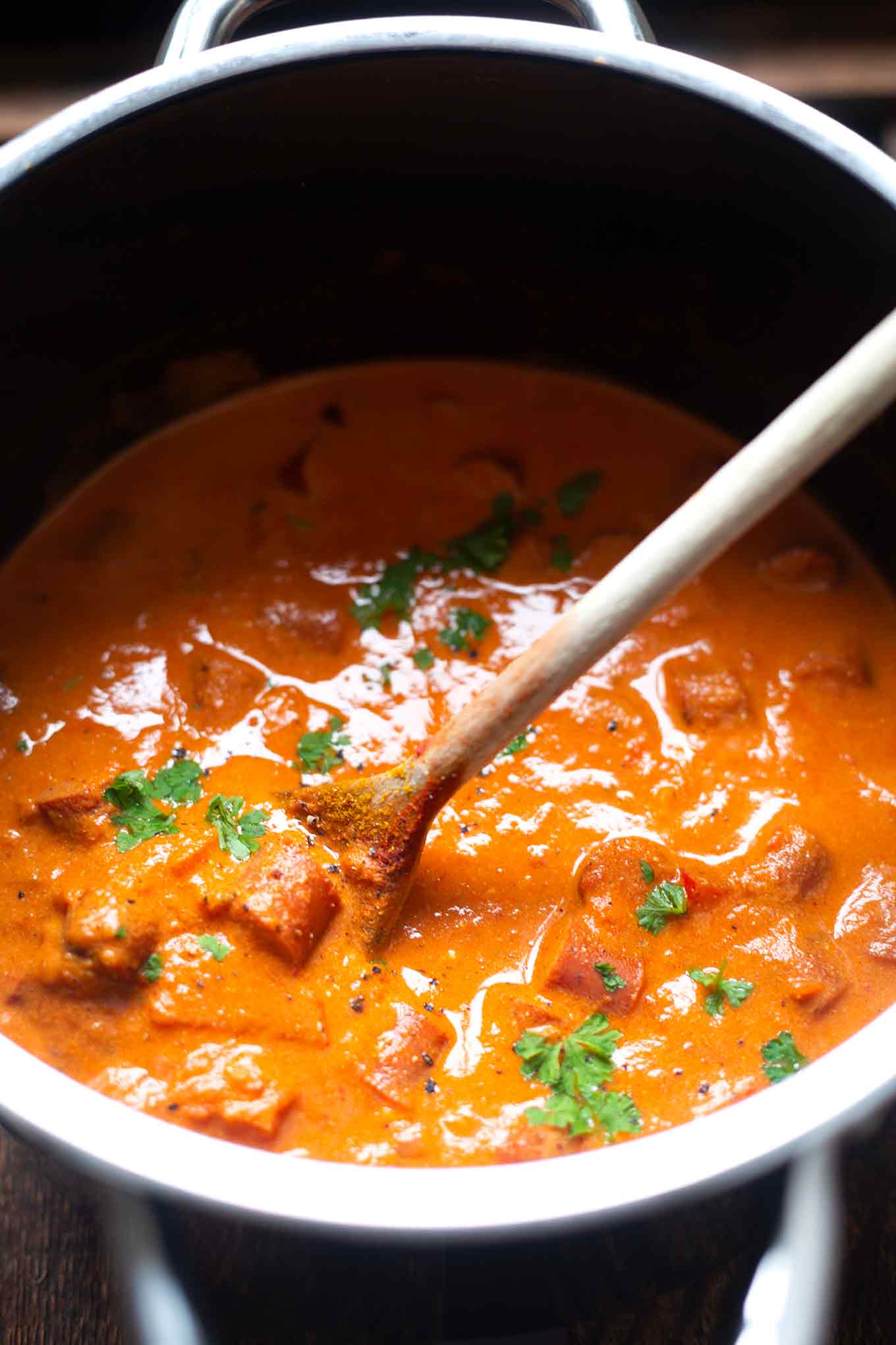 Köchelndes Wurstgulasch in einem Topf mit einem Holzlöffel.