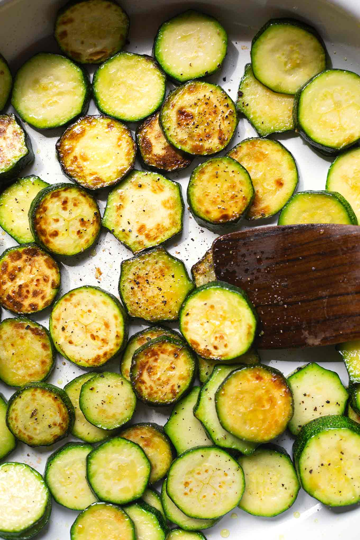 Gebratene Zucchini für die Zucchini-Hack-Pfanne in einer silbernen Pfanne. Die Zucchini-Schreiben werden mit einem Holz-Pfannenwender gewendet,