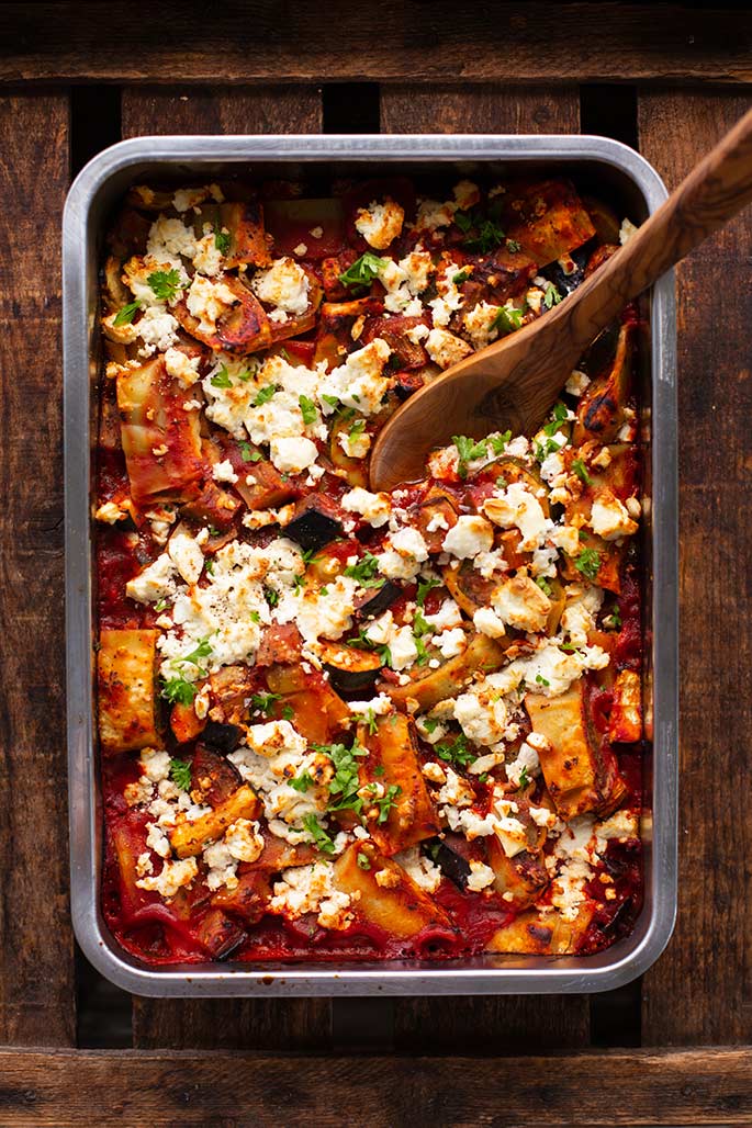 Ratatouille-Auflauf mit Gemüse und Feta in einer Auflaufform, die auf einem Holzuntergrund steht,
