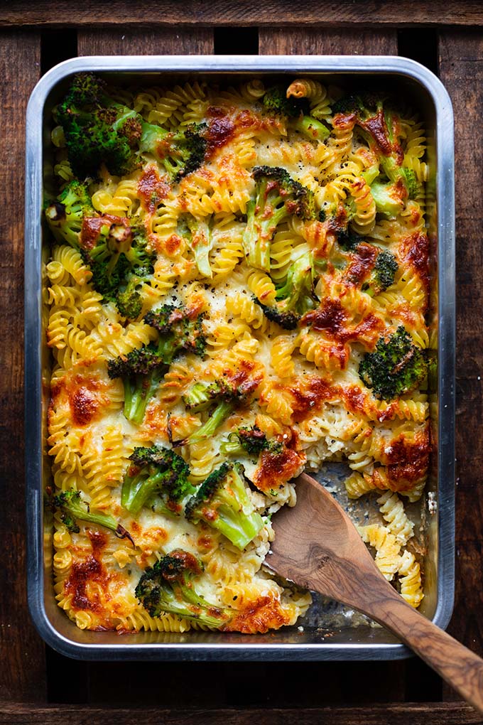 Fertiger Brokkoli-Nudelauflauf in einer Auflaufform auf dunklem Holzuntergrund. Ein großer Holzlöffel bereit zum Servieren.