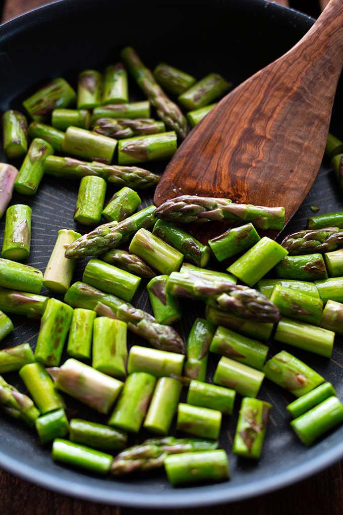 Gebratene Spargelstücke in einer Pfanne mit einem Holzschieber