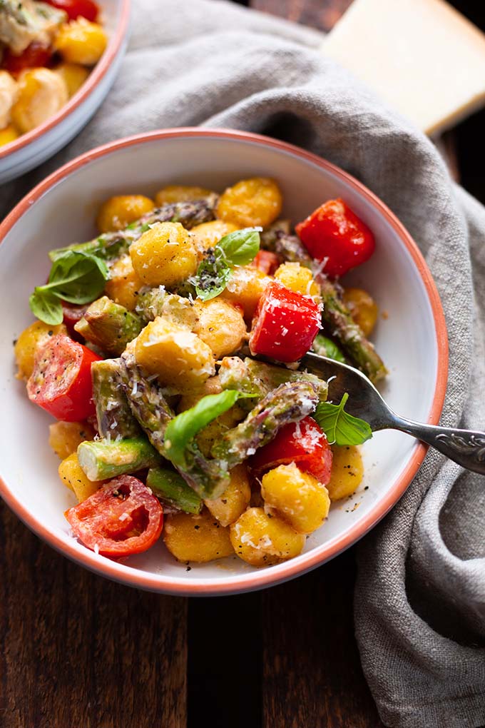 Eine Portion grüner Spargel mit Gnocchi und Tomaten in einer Schüssel, bedeckt mit Parmesan.