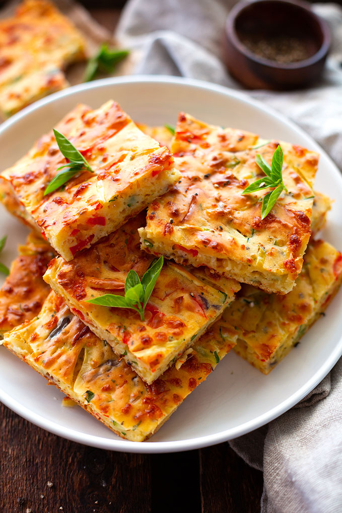 Fertige Gemüse-Quiche in Quadrate geschnitten und auf einem weißen Teller angerichtet.