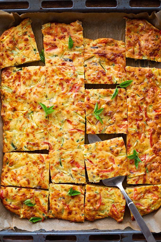 Vegetarische Quiche mit viel Gemüse auf einem Backblech. Geschnitten wie quadratische Kuchen Stücke und mit einem Tortenheber.