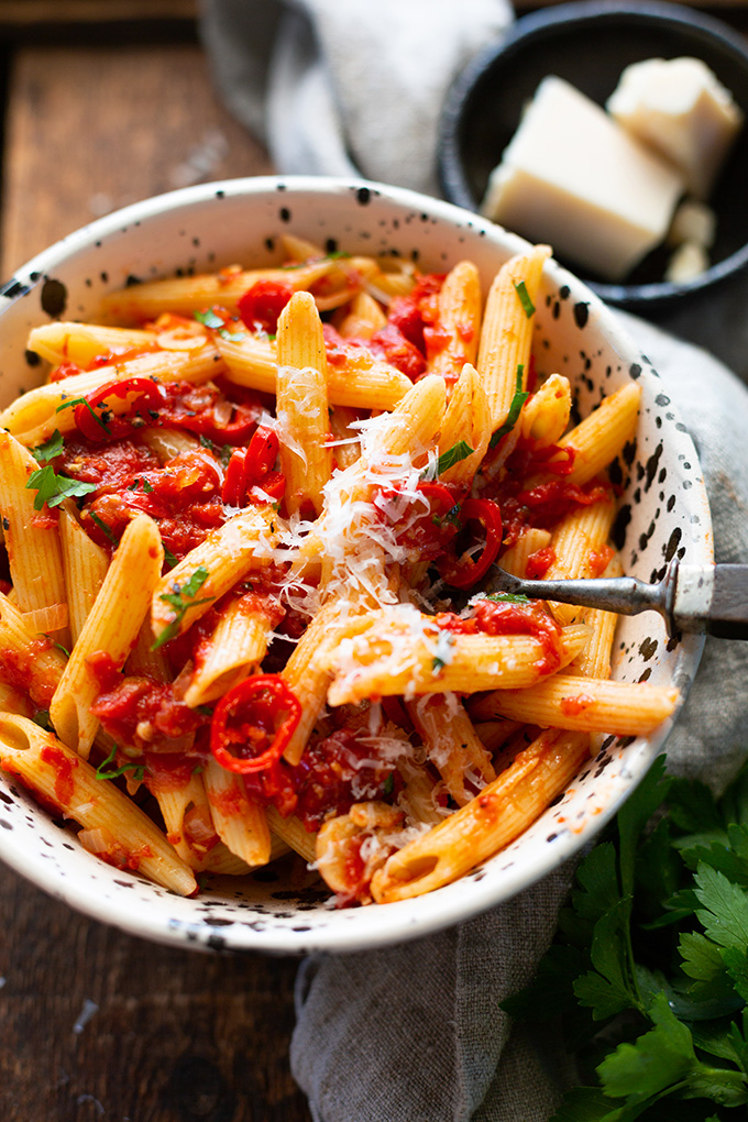 Penne all' Arrabbiata angerichtet in einem weißen Pasta-Teller mit schwarzen Sprenkeln. Garniert mit Parmesan.