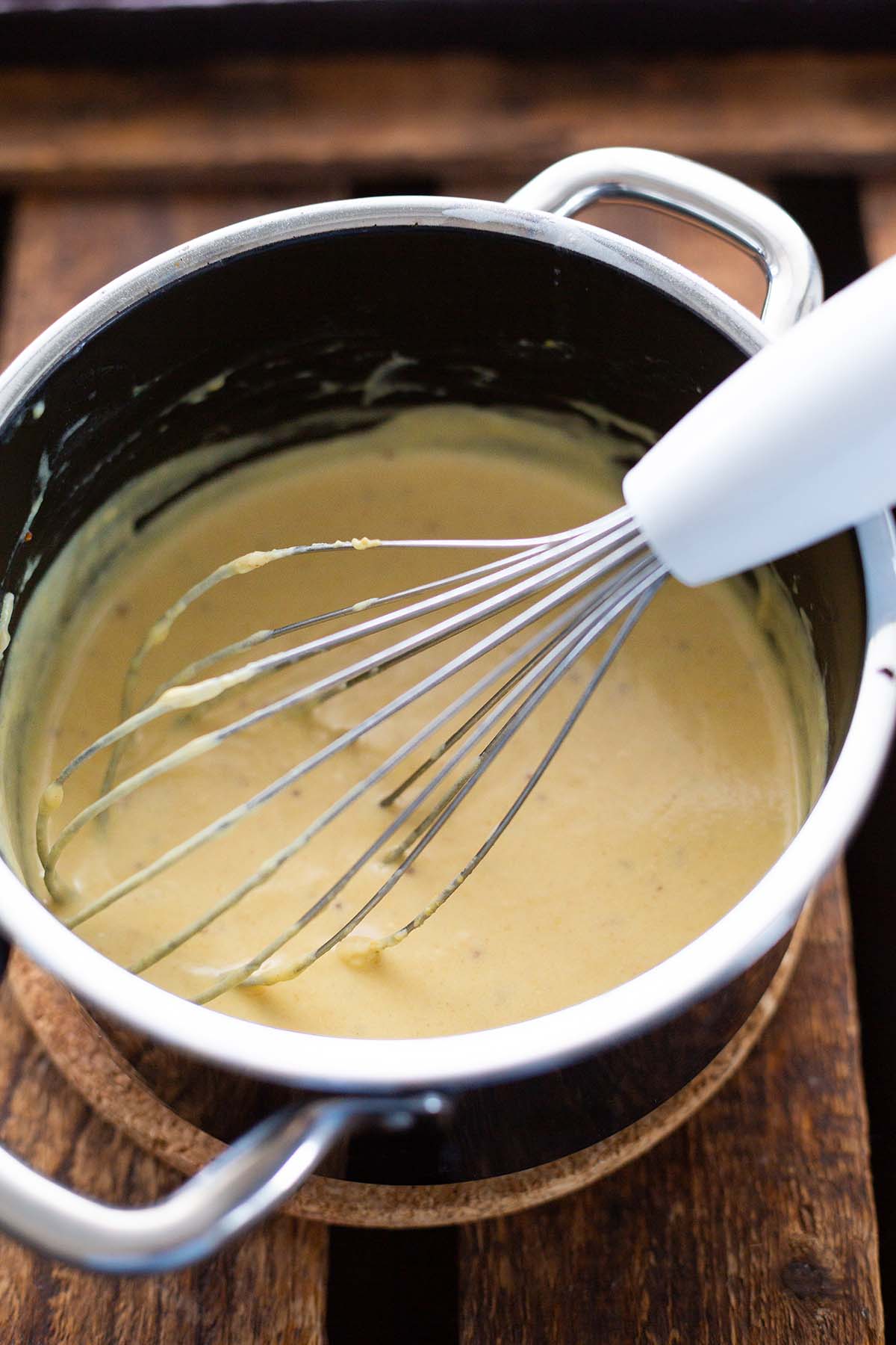 Die Mehlschwitze als Grundlage für die Soße der Senfeier beim Rühren im Kochtopf mit Schneebesen.