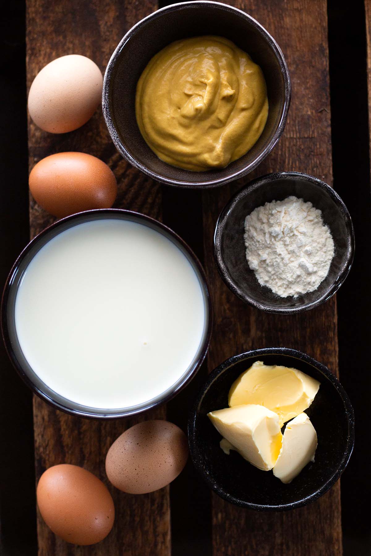 Alle Zutaten für die einfachen Senfeier nach Omas Rezept im Überblick. In kleinen Schüsseln einzeln präsentiert. Zu sehen sind: Eier, Senf, Mehl, Milch, Butter