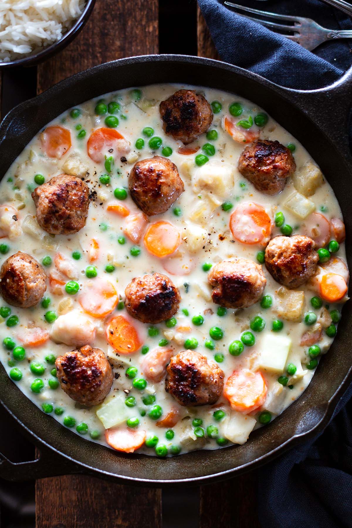 Wikingereintopf mit Fleischbällchen in einer schwarzen Pfanne. Daneben eine Schüssel mit Reis.