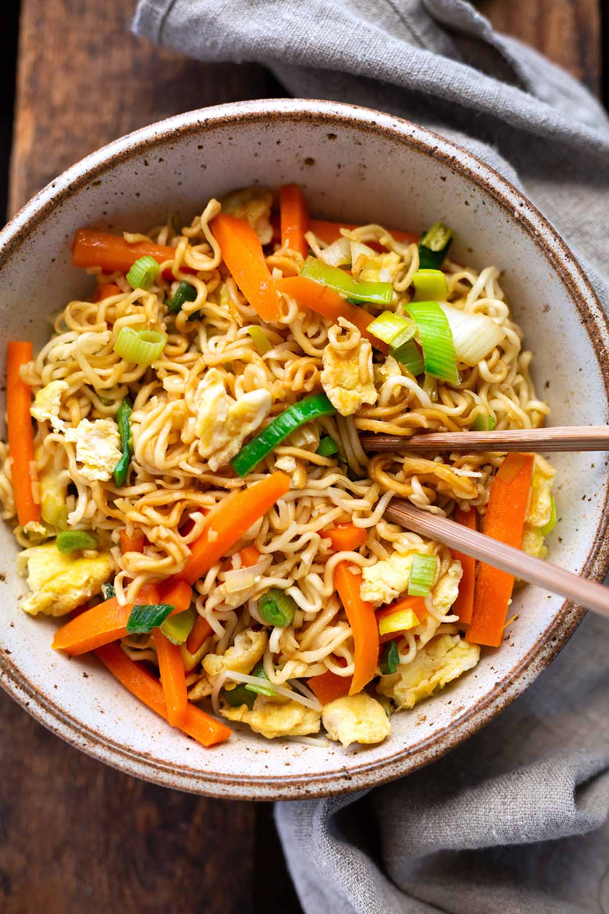 Chinesisch gebratene Nudeln mit Gemüse und Ei mit viel Gemüse in einer Schüssel angerichtet mit Essstäbchen.