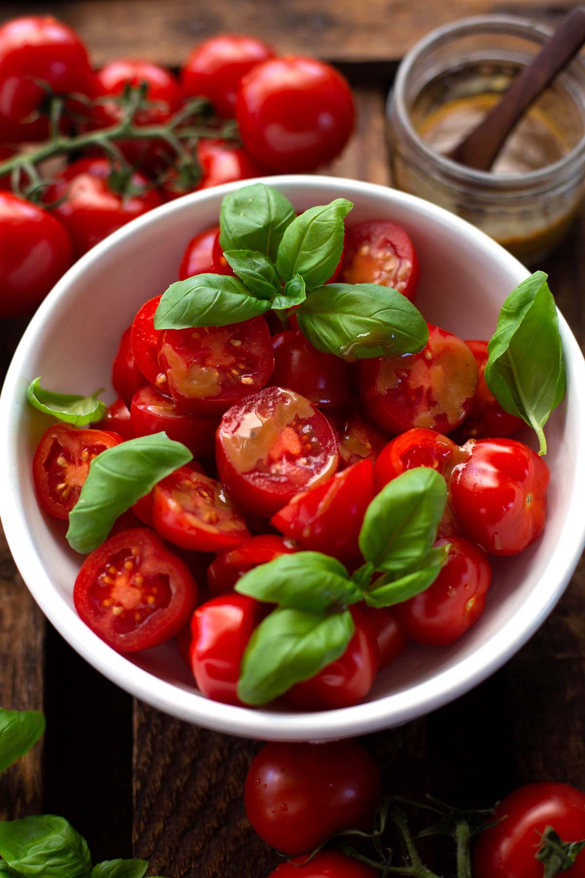 Frische, rote Cherrytomaten mit Basilikum und Balsamico-Dressing in einer weißen Schüssel.