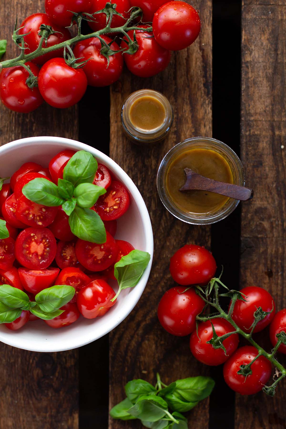 Schnelles Balsamico-Dressing in einem Marmeladenglas mit einem Löffel angerichtet mit frischen Tomaten und Basilikum in einer weißen Schüssel.
