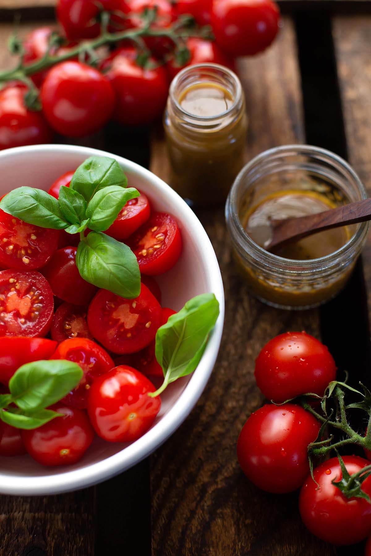 Schnelles Balsamico-Dressing in einem Marmeladenglas mit einem Löffel angerichtet mit frischen Tomaten und Basilikum in einer weißen Schüssel.