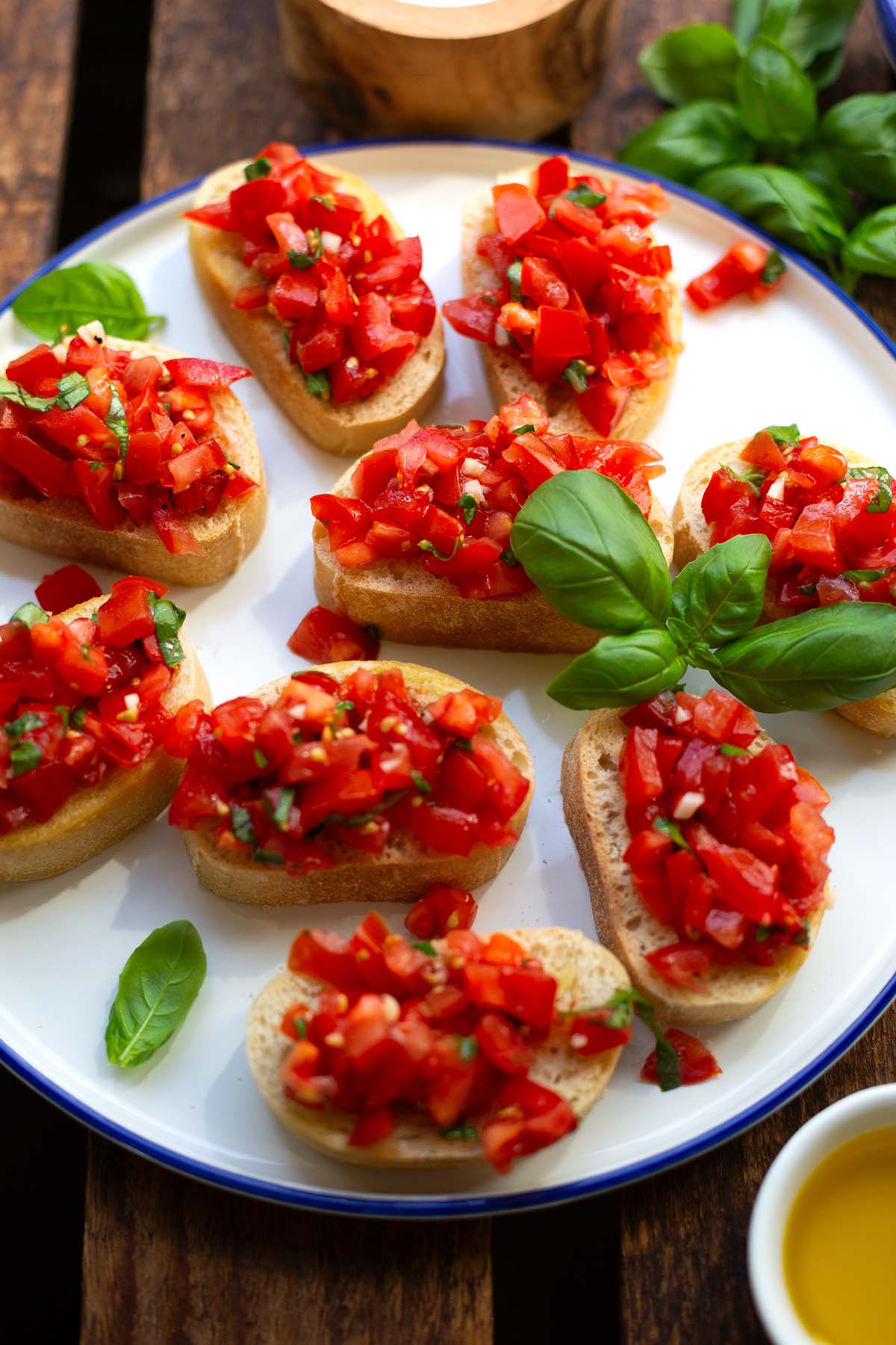 Italienische Bruschetta angerichtet mit Basilikum auf einem weißen Teller mit blauem Rand.