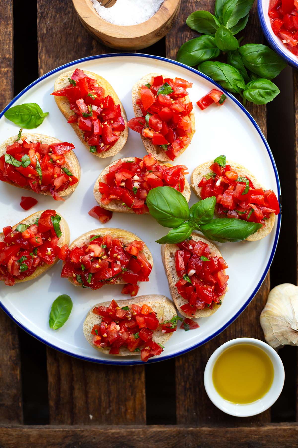 Italienische Bruschetta angerichtet mit Basilikum auf einem weißen Teller mit blauem Rand.