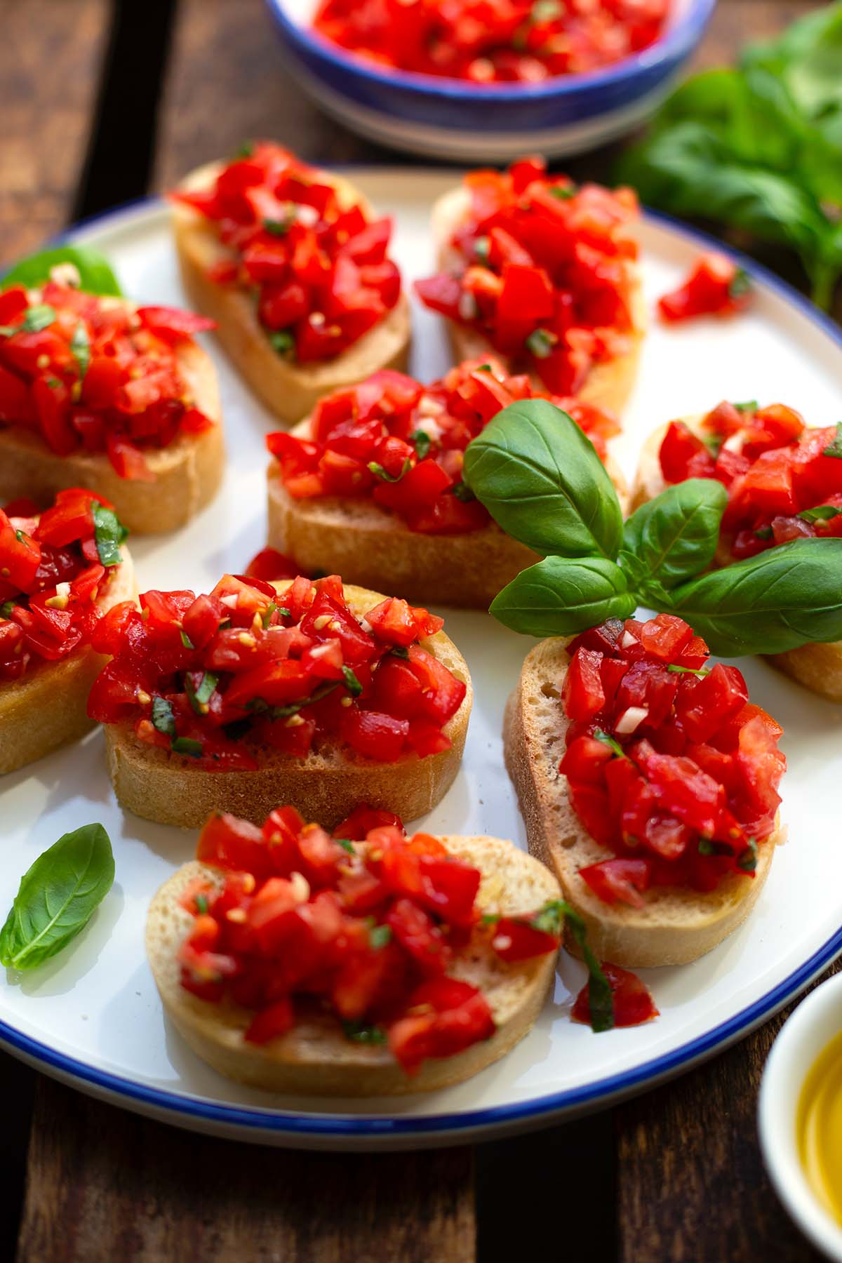 Italienische Bruschetta im Close-up angerichtet mit Basilikum auf einem weißen Teller mit blauem Rand.