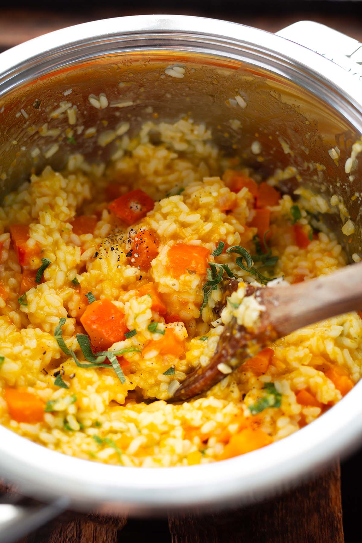 Kürbisrisotto mit Salbei & Parmesan in Nahaufnahme im Topf mit einem Holzlöffel.