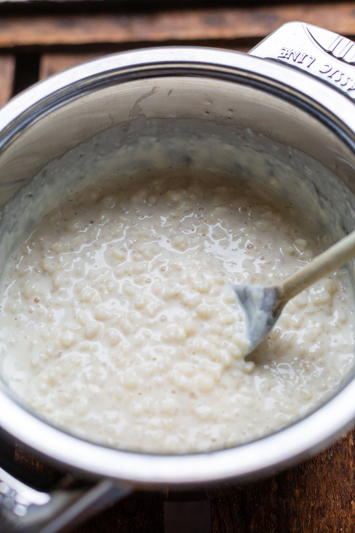 Milchreis im silbernen Edelstahl Topf mit einem Holzlöffel