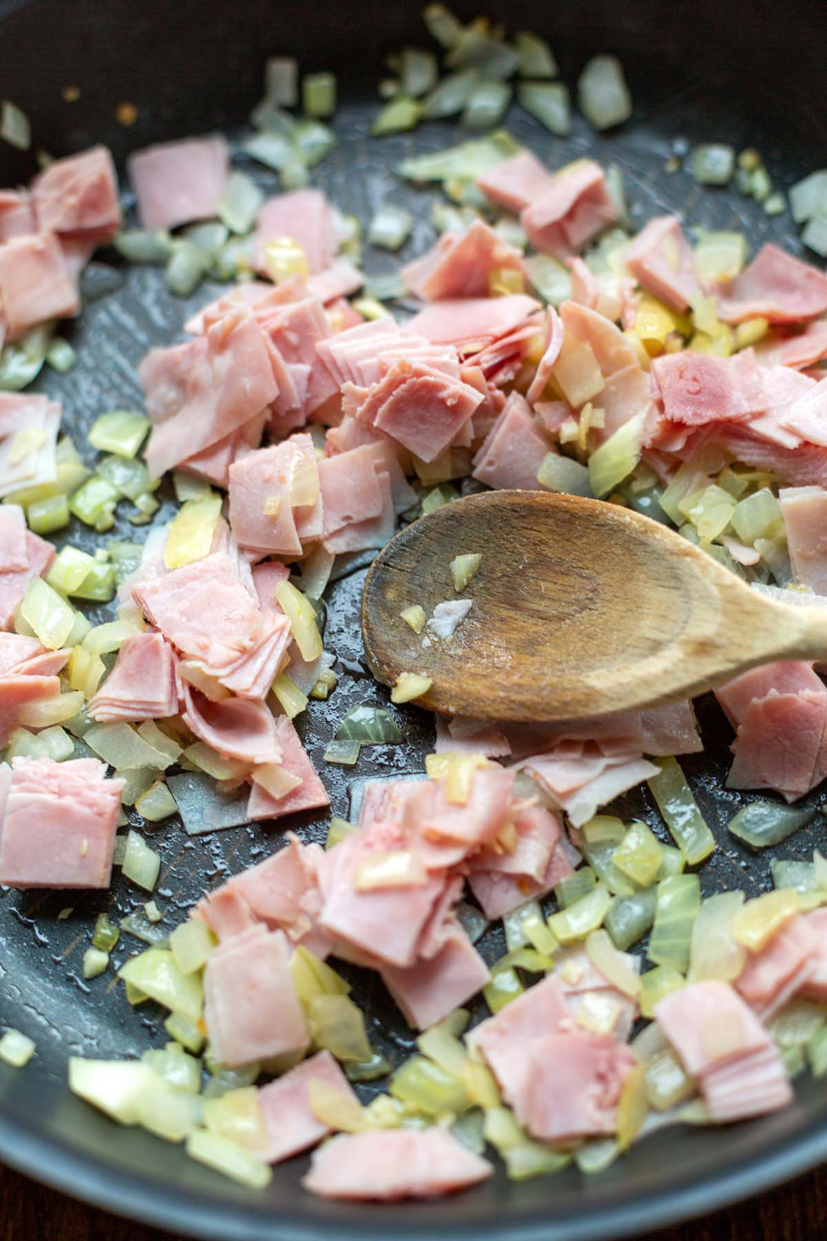 Schinken & Zwiebeln beim Anbraten in einer beschichteten Pfanne mit einem Holzlöffel.