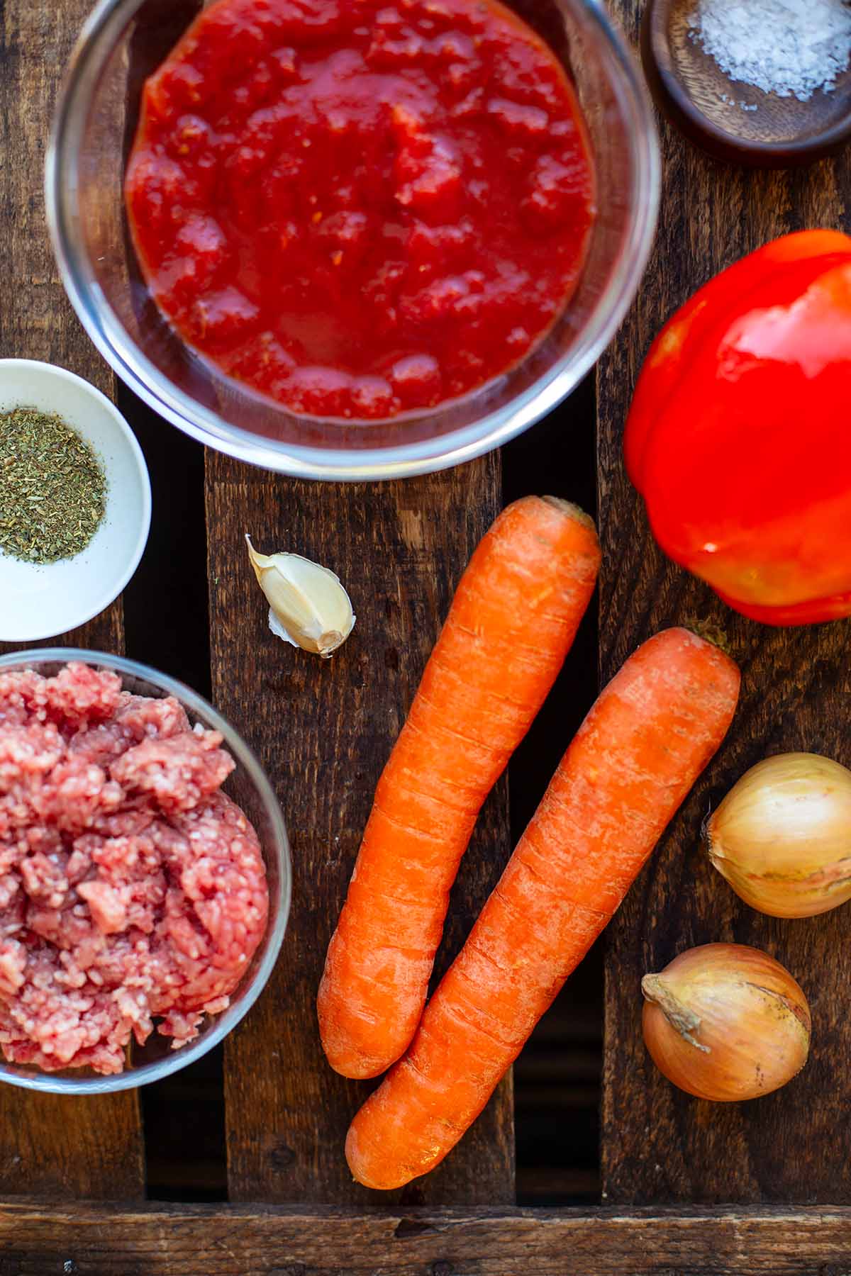 Zutaten für Hackfleischsoße in kleinen Schüssel einzeln aufbewahrt. Zu sehen sind Tomaten, Paprika, Salz, italienische Kräuter, Karotten, gemischtes Hackfleisch, Knoblauch und Zwiebeln.