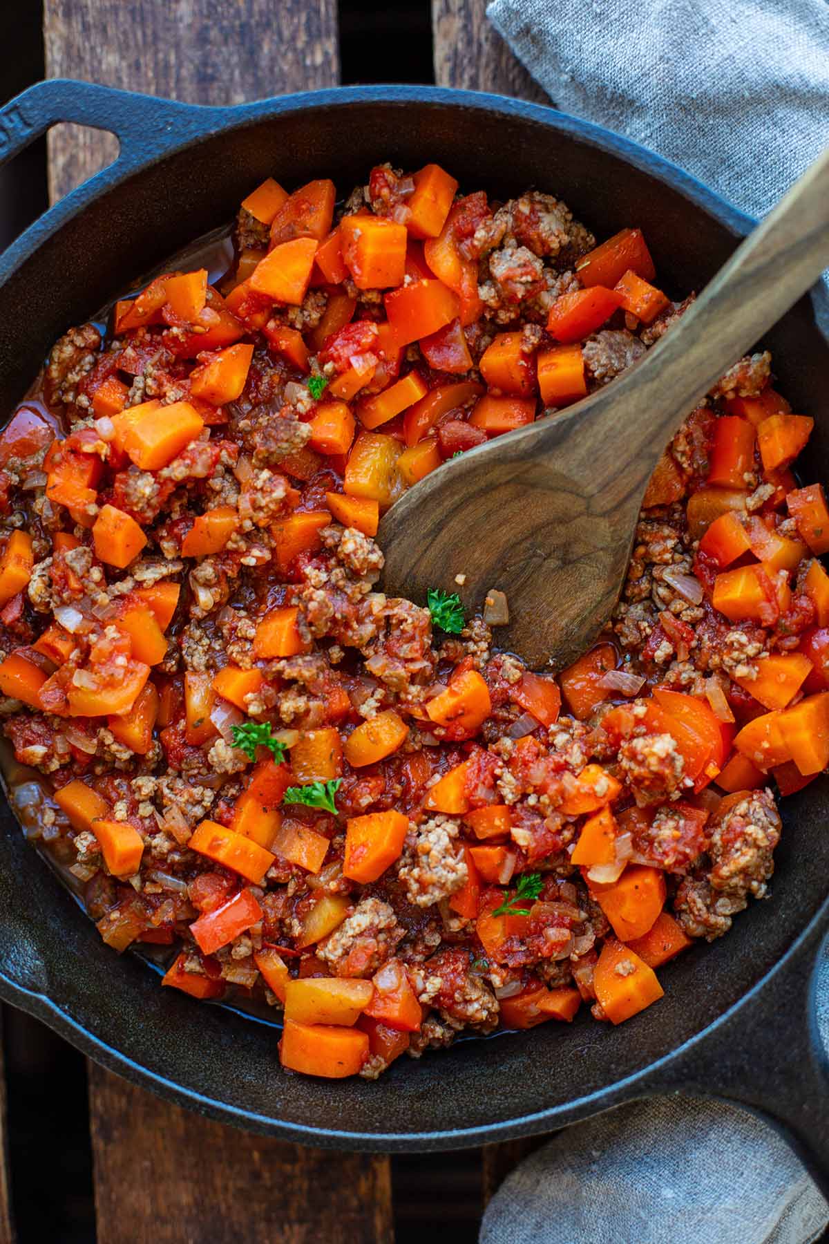 Hackfleischsoße mit Tomaten in einer Gusseisernen Pfanne mit Holzlöffel.