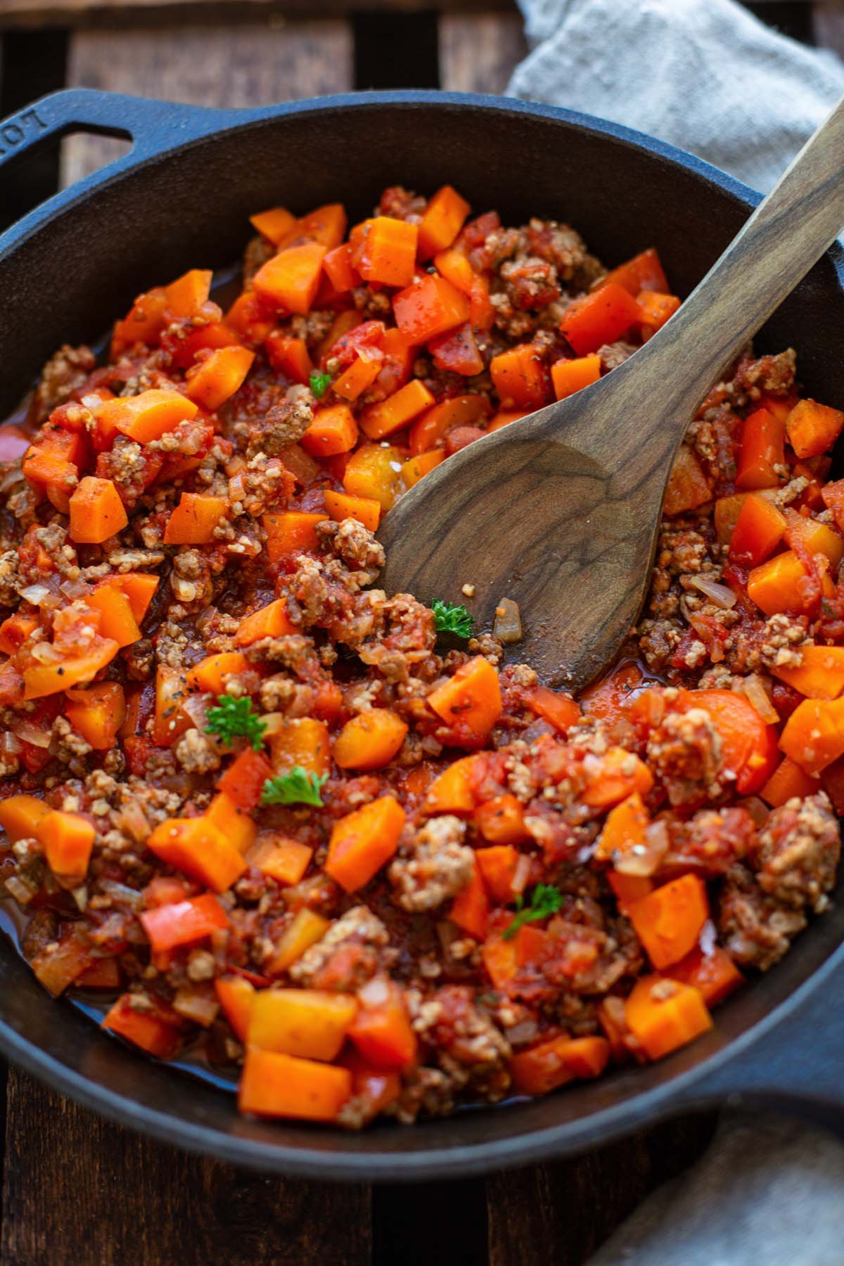 Hackfleischsoße mit Tomaten und Gemüse in einer Gusseisernen Pfanne mit Holzlöffel.