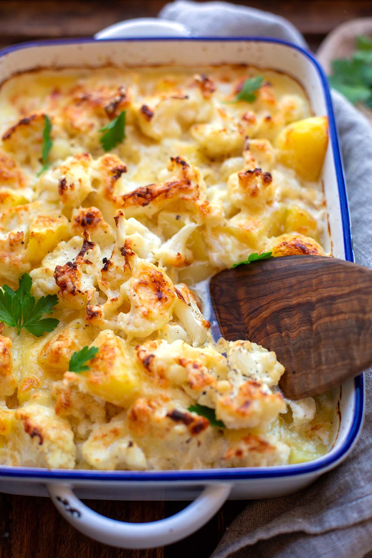 Blumenkohl-Auflauf mit Kartoffeln & cremiger Käse-Sahne-Soße in einer weißen Emaillie-Auflaufform mit blauem Rand.
