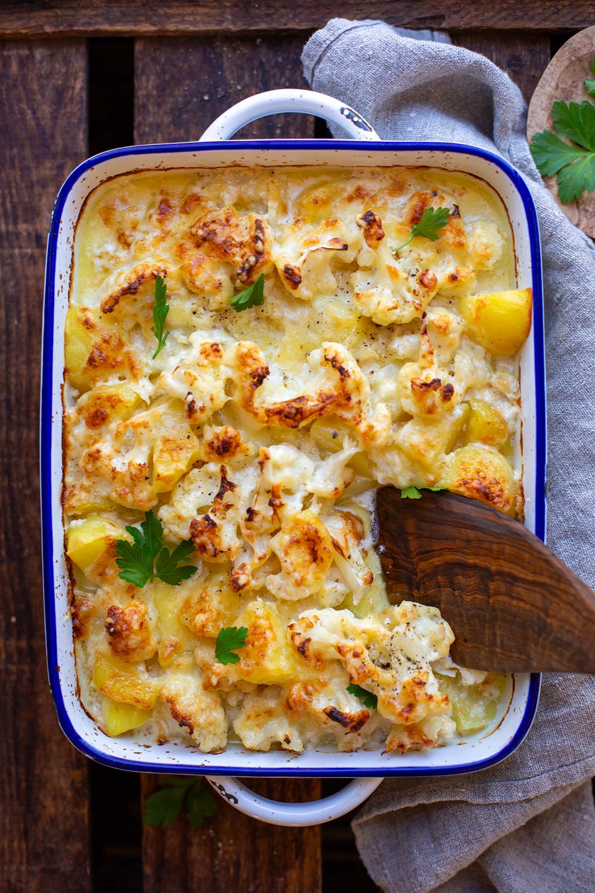 Blumenkohl-Auflauf mit knuspriger Käse-Kruste nach dem Backen. in einer weißen Emaillie-Auflaufform mit blauem Rand.