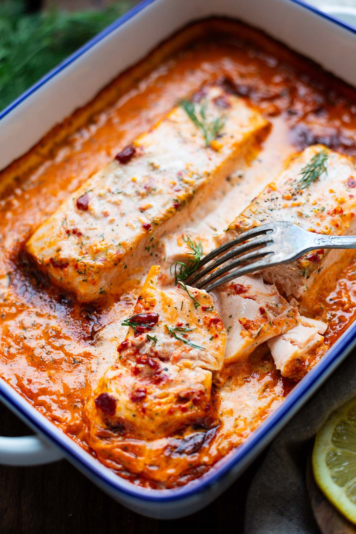 Lachs-Sahne-Gratin aus dem Ofen in einer Tomaten-Sahne-Soße in einer weißen Emaille-Form mit blauem Rand mit Dill garniert.