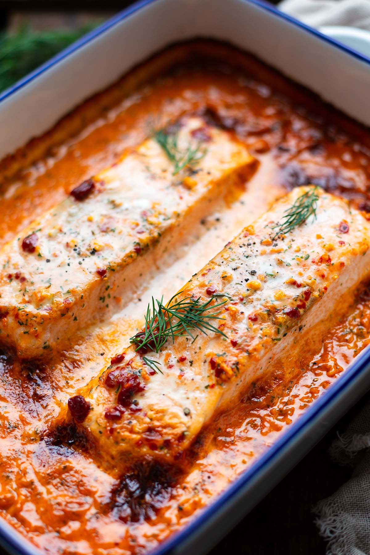 Lachs-Sahne-Gratin aus dem Ofen in einer Tomaten-Sahne-Soße in einer weißen Emaille-Form mit blauem Rand mit Dill garniert.
