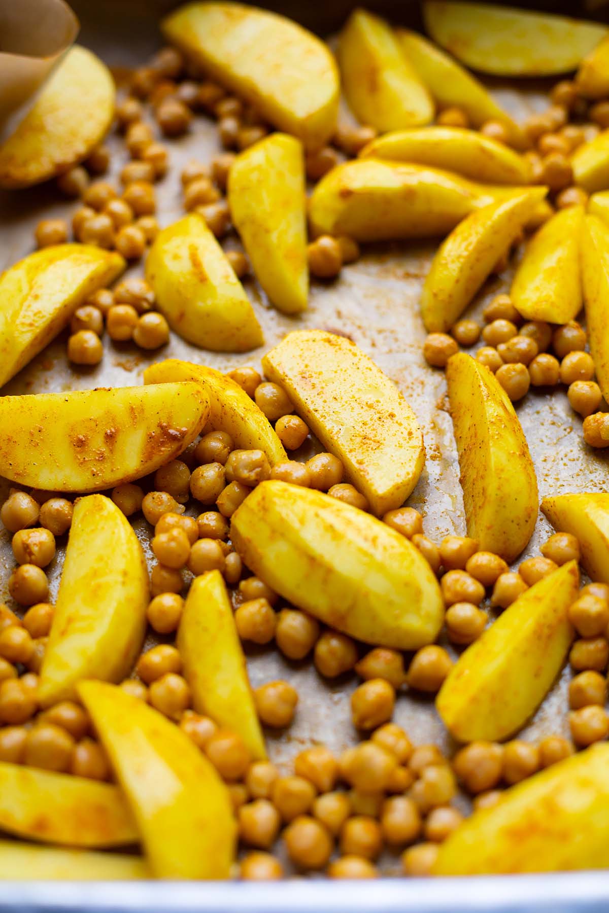 Marinierte Curry Kartoffeln und Kichererbsen vor dem Rösten auf einem Backblech im Close up.