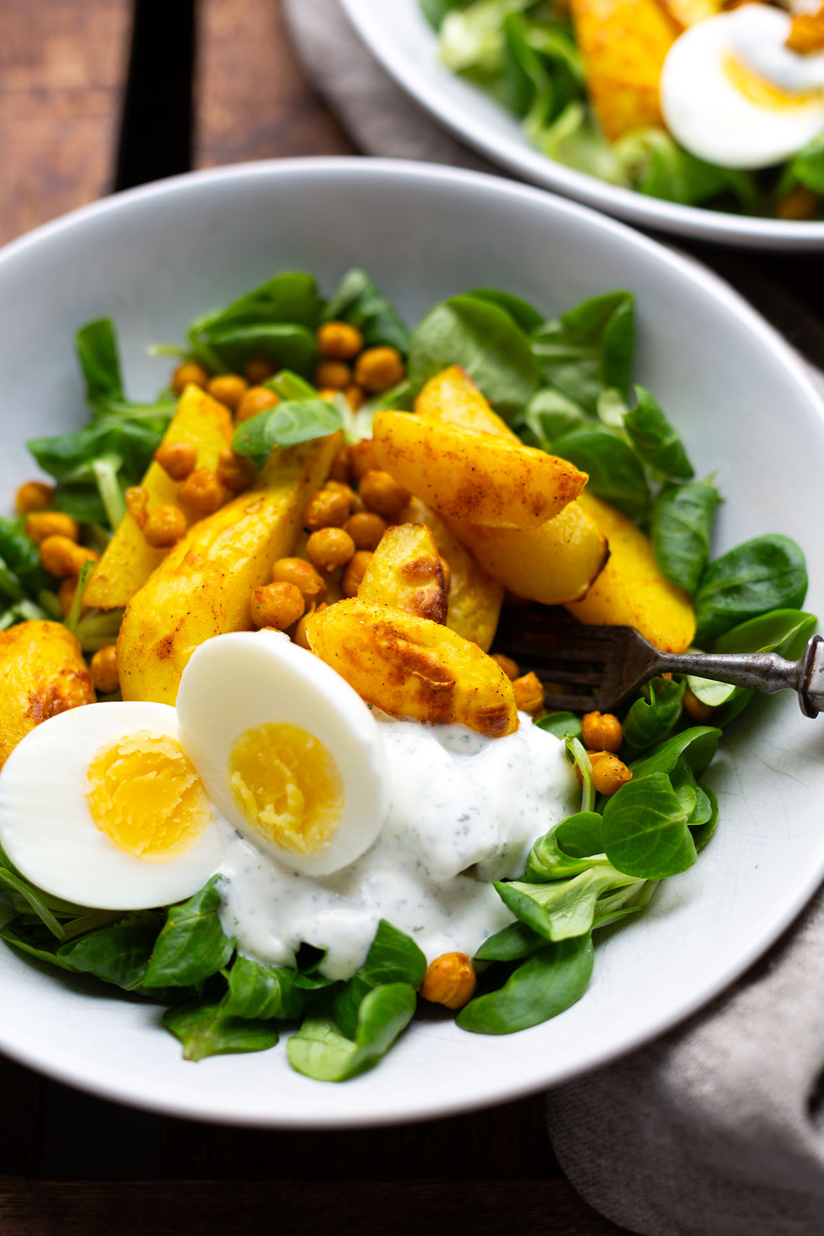 Salat Bowl mit Kichererbsen, gerösteten Kartoffel und Quark-Dressing in einer weißen Schüssel angerichtet mit einem gekochten Ei und Feldsalat.