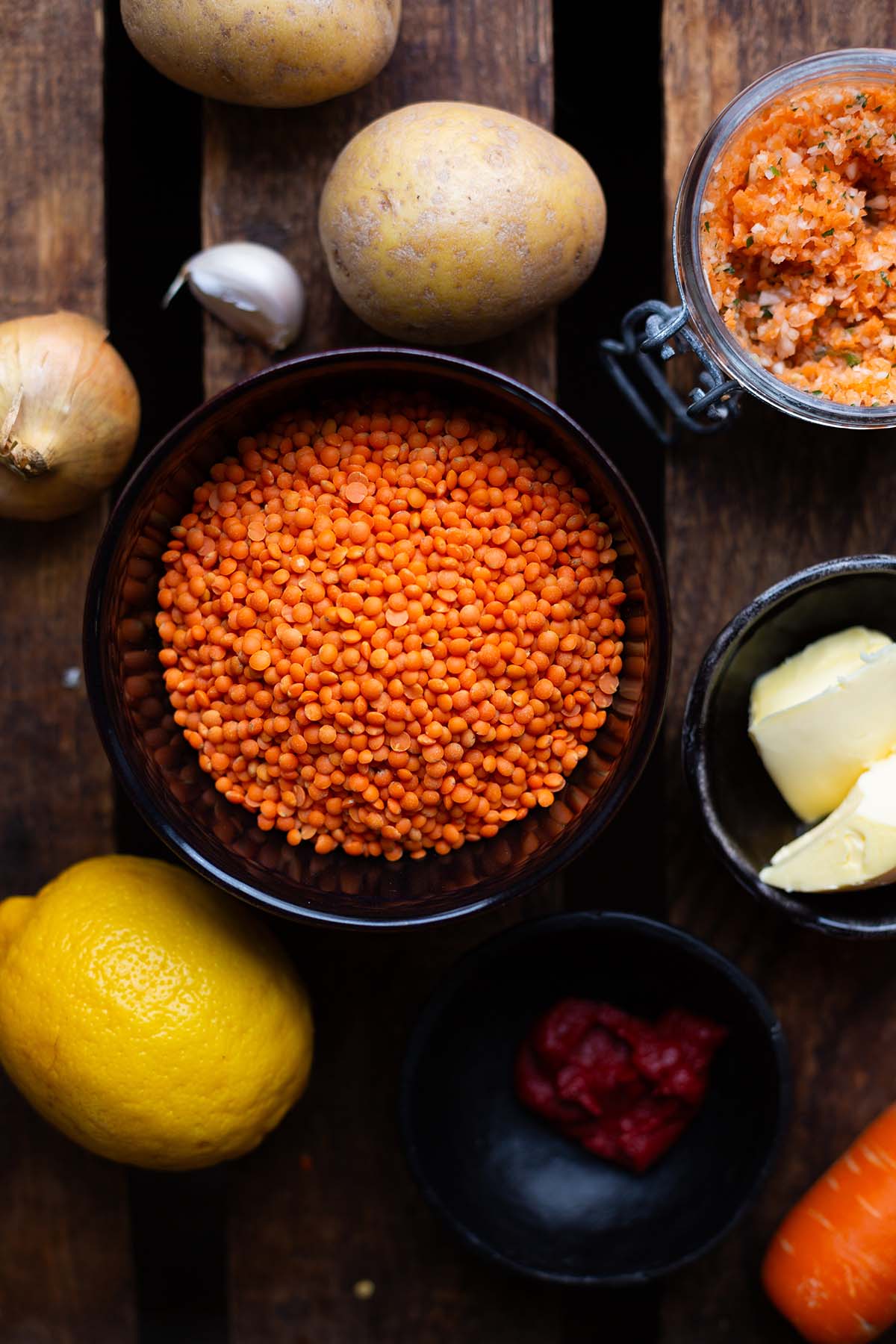 Zutaten für die türkische Linsensuppe in kleinen Schalen. Zu sehen sind: rote Linsen, Zwiebeln und Knoblauch, Zitrone, Kartoffeln, Gemüsebrühe, Tomatenmark, Gemüsebrühe und Butter