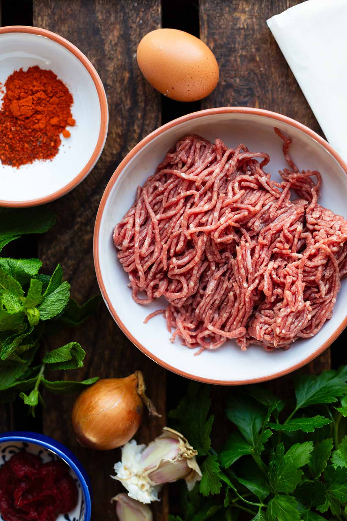 Die Zutaten für Sigara Börek einzeln in Schüssel präsentiert. Zu sehen sind: Hackfleisch, Ei, Gewürze, Zwiebeln & Knoblauch, Tomatenmark, Petersilie & Minze.