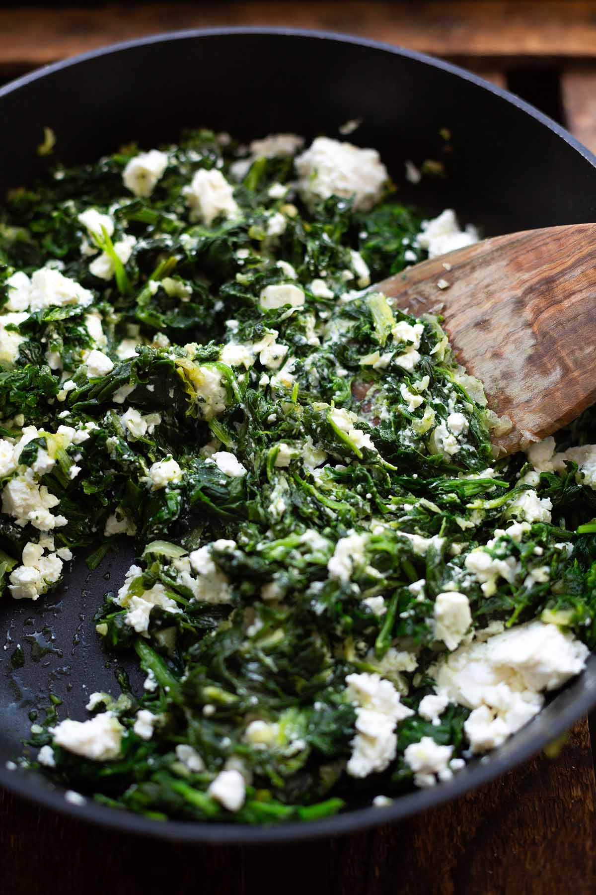 Börek-Füllung mit Spinat und Feta in einer schwarzen Pfanne mit einem Kochlöffel