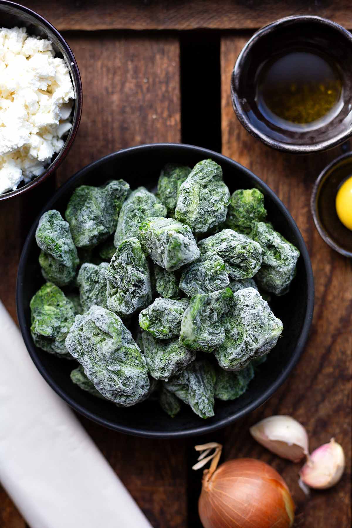 Zutaten für Börek in Schüsseln auf einer Holzkiste: Spinat, Feta, Olivenöl, Eigelb, Yufkateig, Zwiebel und Knoblauch