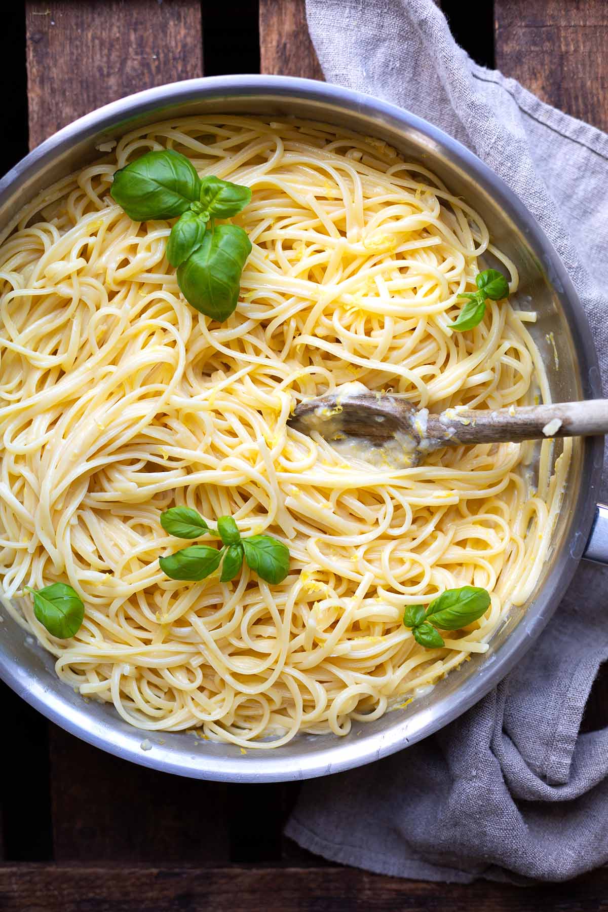 Fertig gekochte Pasta al limone in einem Topf auf dunklem Holzuntergrund, garniert mit Basilikum und mit einem Holzlöffel.