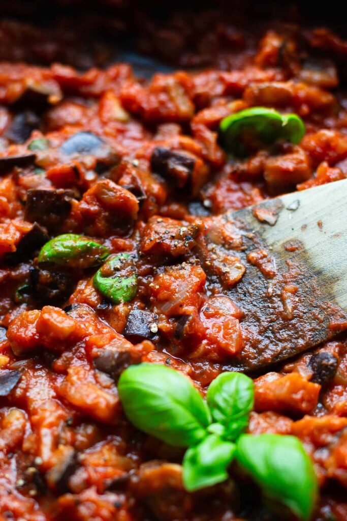 Fertige Pasta alla Norma in einer Pfanne mit einem Pfannenwender. Garniert mit Basilikum.