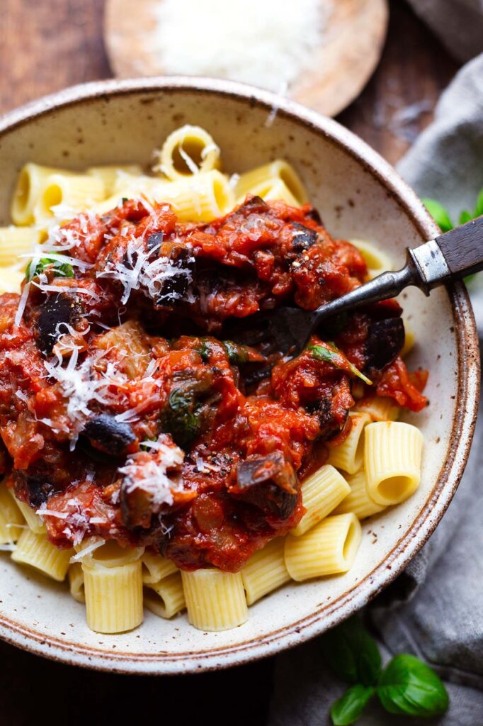 Fertige Pasta alla Norma in einer Schüssel und einer Gabel. Garniert mit geriebenem Parmesan.