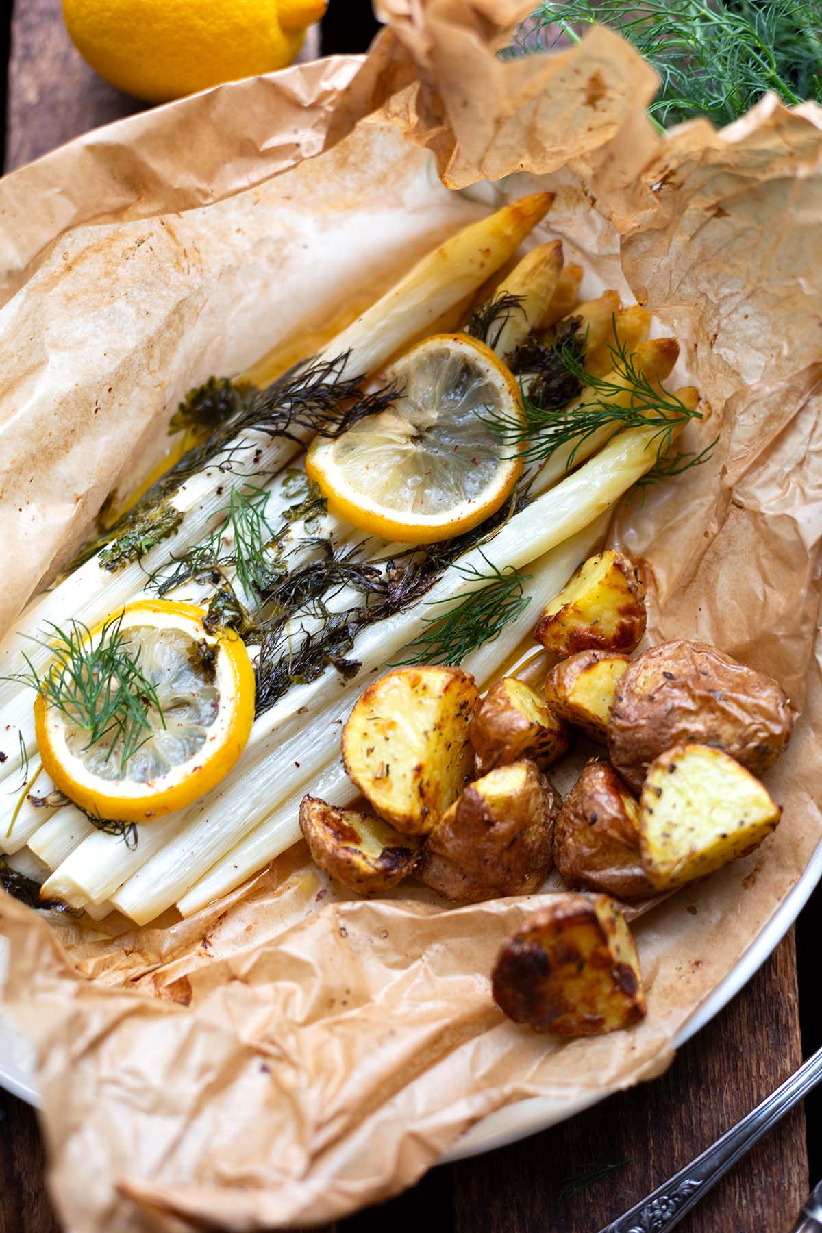 Fertiger weißer Spargel aus dem Backofen. Liegt noch auf Backpapier eingewickelt und garniert mit Zitronenscheiben, Dill und Ofenkartoffeln.