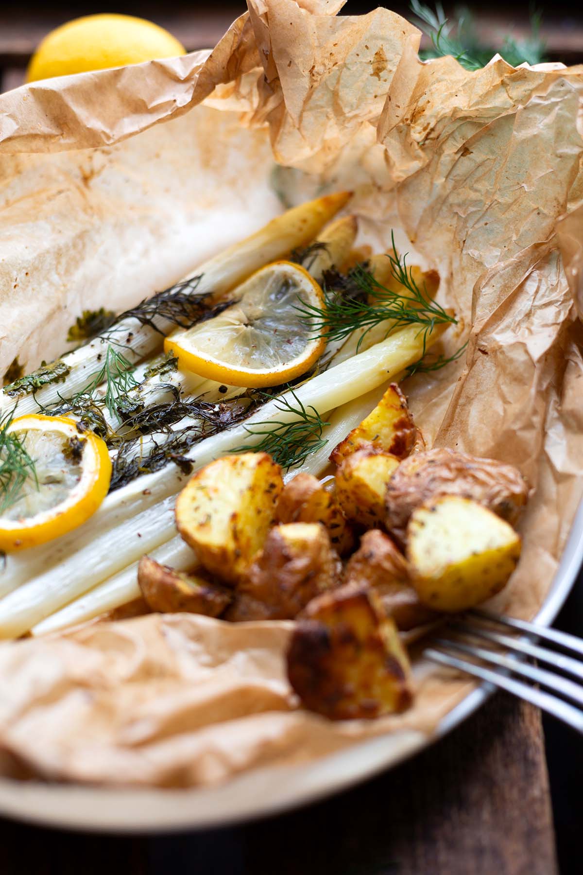 Fertiger weißer Spargel aus dem Backofen. Liegt noch auf Backpapier und garniert mit Zitronenscheiben, Dill und Ofenkartoffeln.
