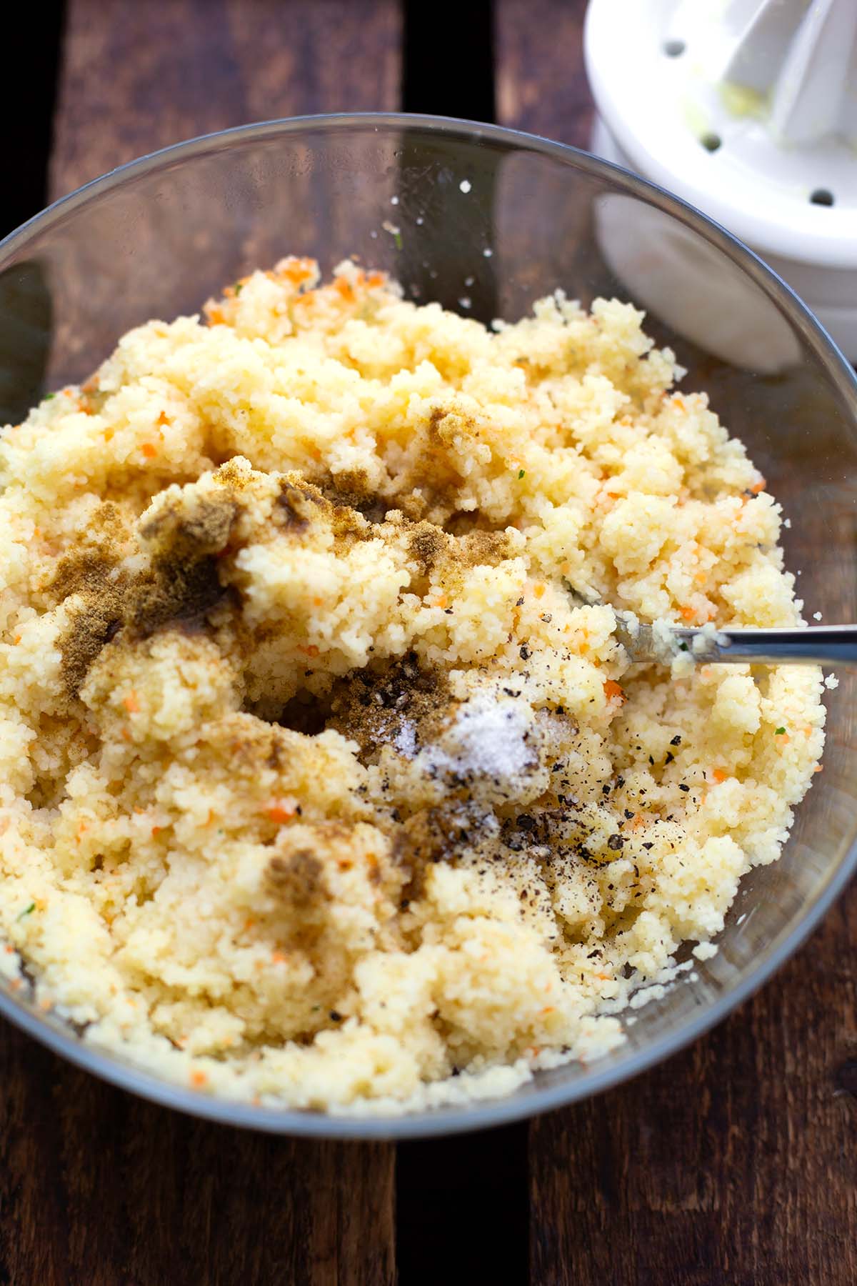 In Gemüsebrühe aufgequellter Couscous in einer Glasschüssel mit Gewürzen drauf, kurz vor dem Umrühren.