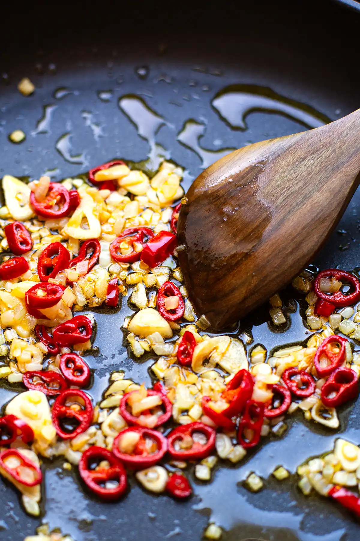 Klein geschnittene Zwiebeln, Chili und Knoblauch werden in Olivenöl in einer scharzen Pfanne für Arrabbiata Sauce angebraten und mit einem Pfannenwender aus Holz gewendet.